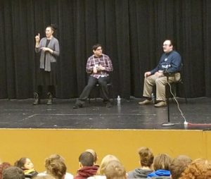 Tim McCue and Noah Seidel standing on a stage with an interpreter, in front of an audience.